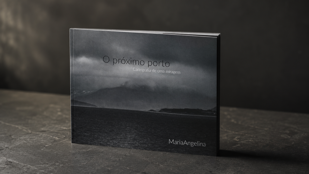 Livro O próximo porto — Cartografia de uma miragem, de MariaAngelina, apresentado sobre uma superfície escura.