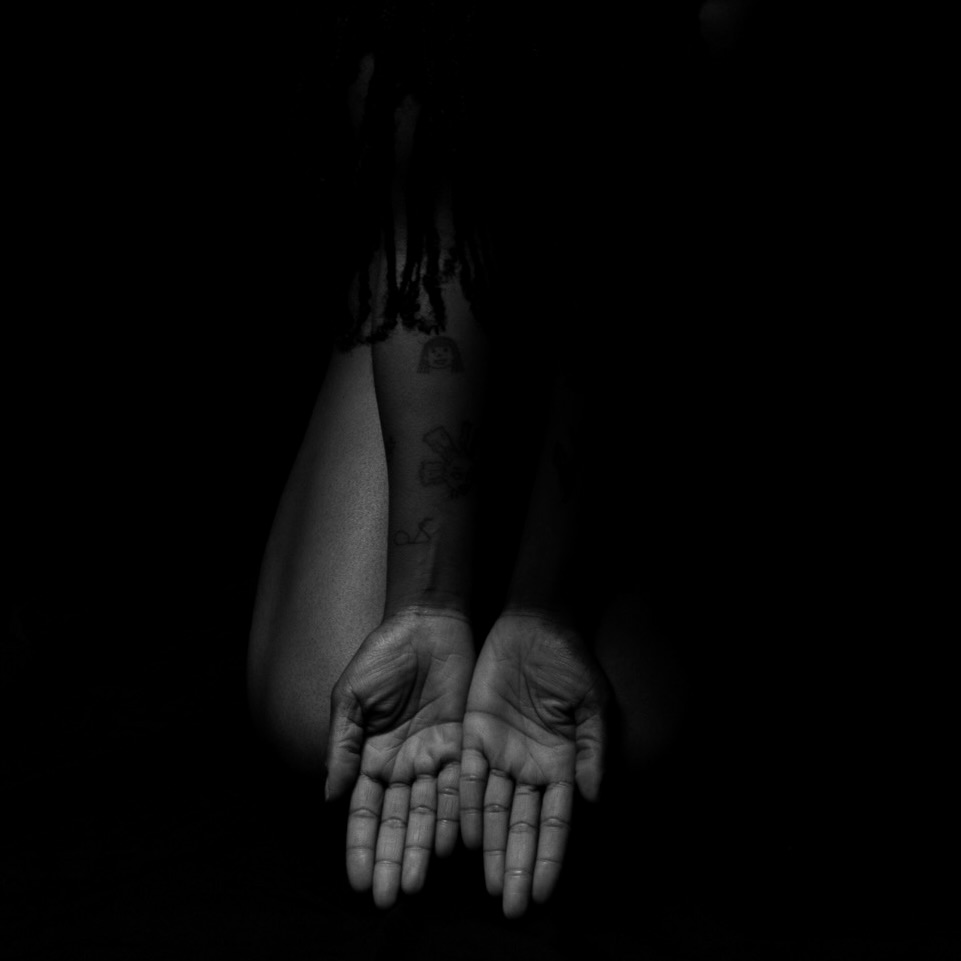 Duas mãos abertas voltadas para cima, iluminadas contra um fundo negro, numa fotografia a preto e branco.